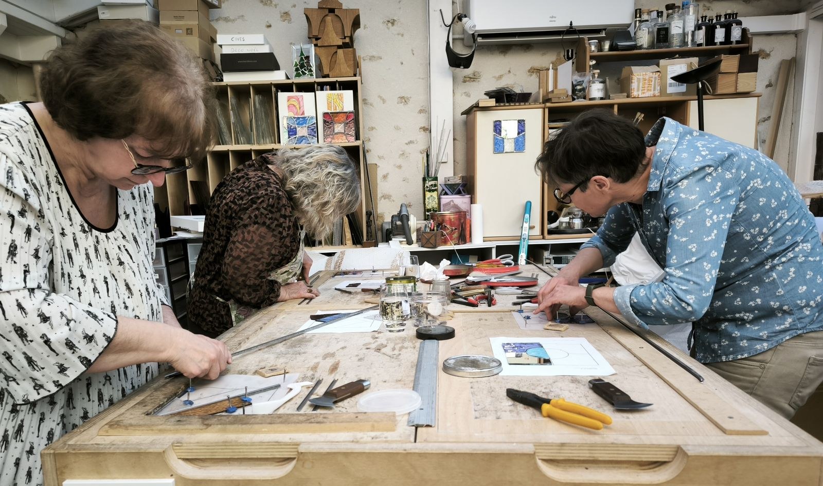 Trois participantes apprenant les gestes du vitrail autour d’une table d’atelier